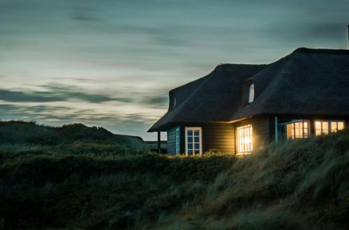 gray house with fireplace surrounded by grass under white and gray cloudy sky