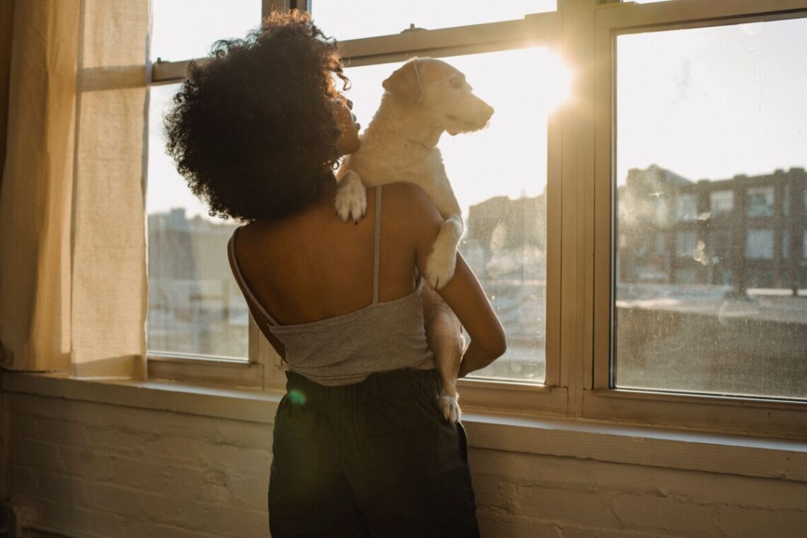 black woman holding dog near window